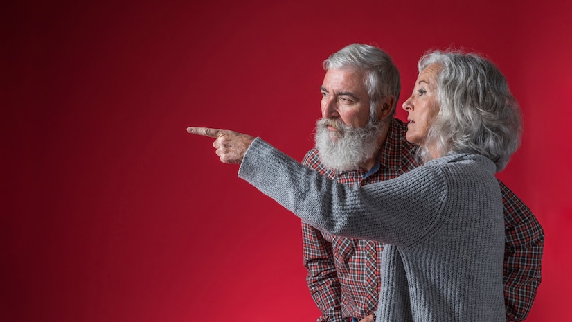 senior-woman-showing-something-her-husband-by-pointing-finger-against-red-background_23-214809...jpg